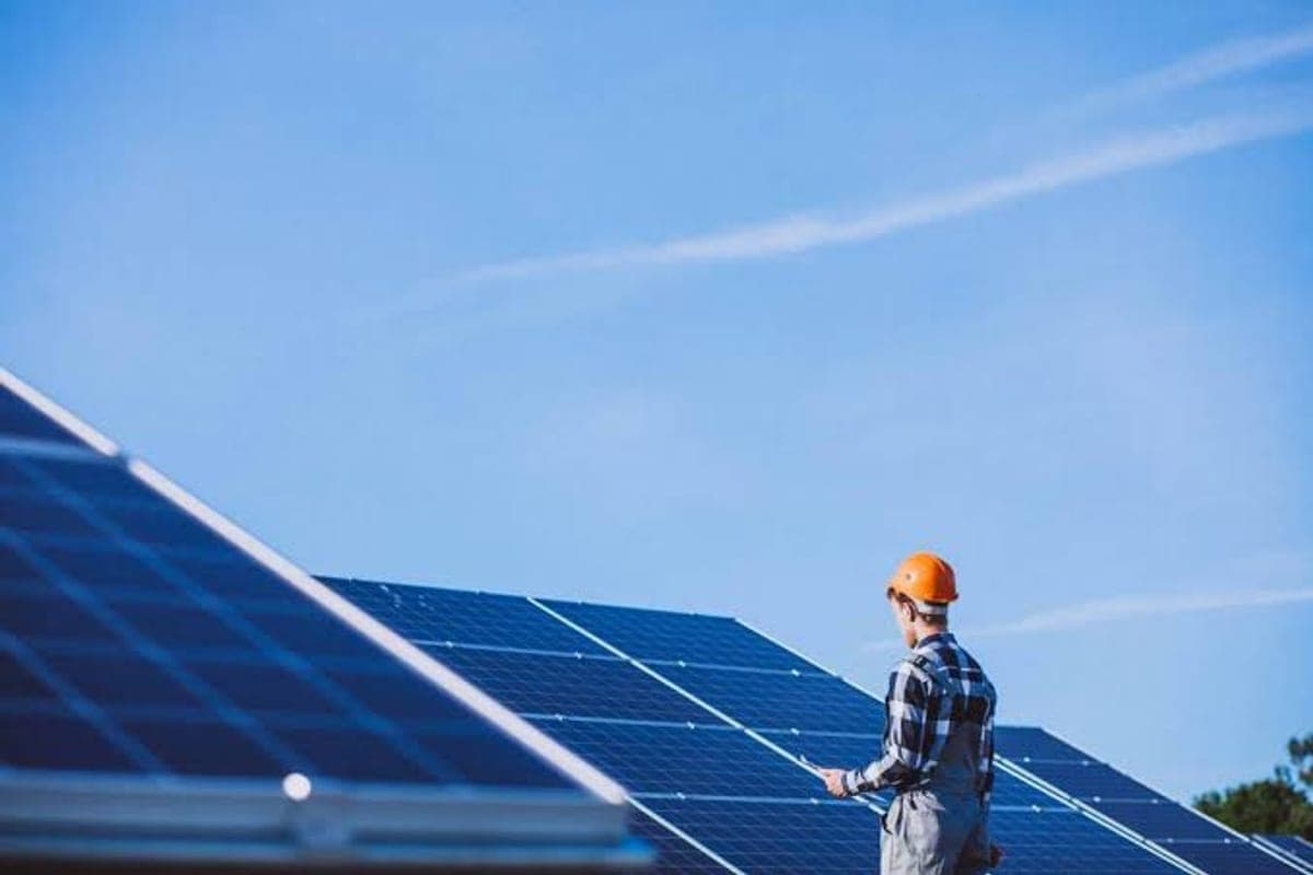 Técnico de capacete em um telhado com painéis solares fotovoltaicos sob céu azul.