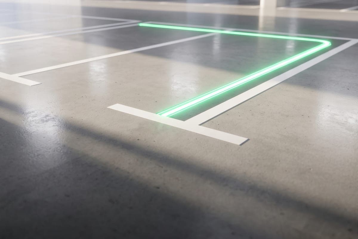Vaga de estacionamento demarcada no piso de concreto, com o contorno realçado por uma linha de luz verde.